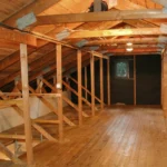 Fotografie půdy s trámy a dřevěnou podlahou.