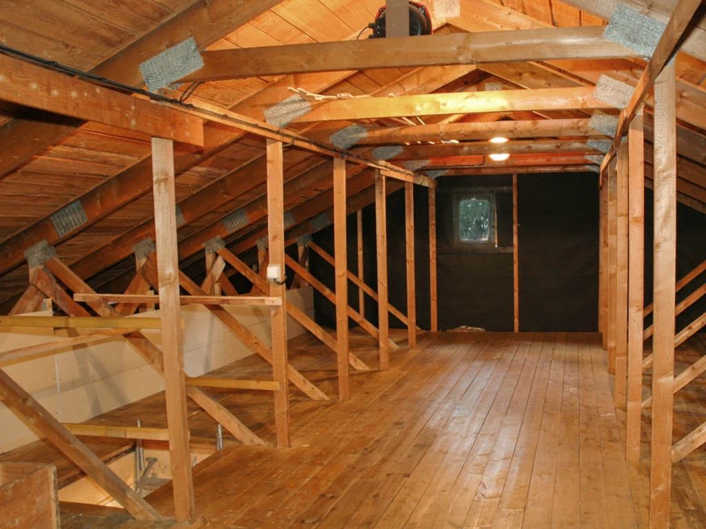 Fotografie půdy s trámy a dřevěnou podlahou.